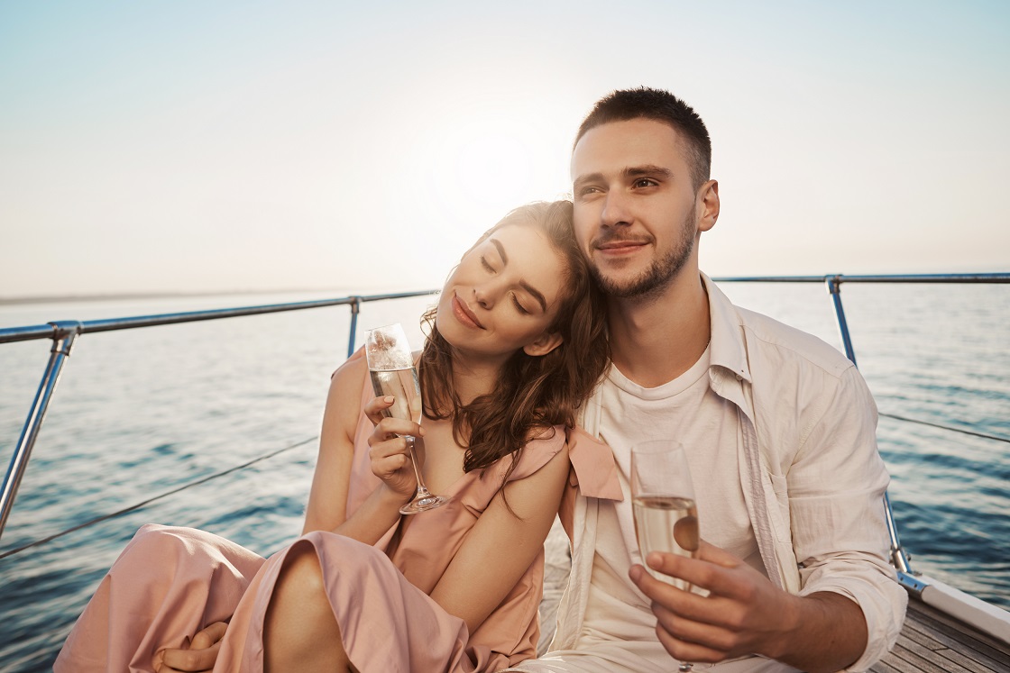 outdoor-portrait-of-adult-happy-male-and-female-in-love-celebrating-their-engagement-on-yacht-holding-glass-of-champagne-and-hugging-boyfriend-just-told-about-things-he-likes-in-her